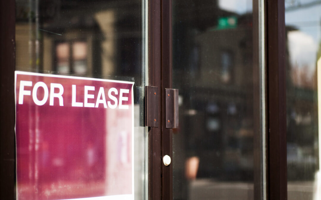 A close up of a sign reading "For Lease" in the window of a vacant commercial property.